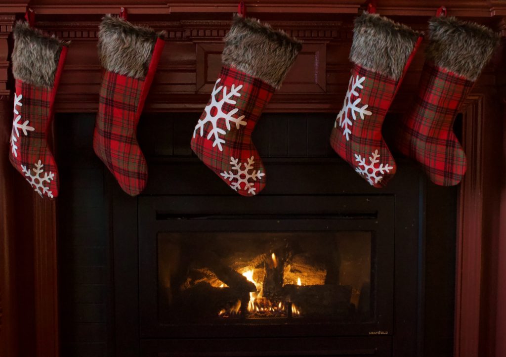 5 plaid Christmas stockings hanging on fireplace mantel with a fire going in fireplace. 60 Dollar Tree Stocking Stuffer ideas.