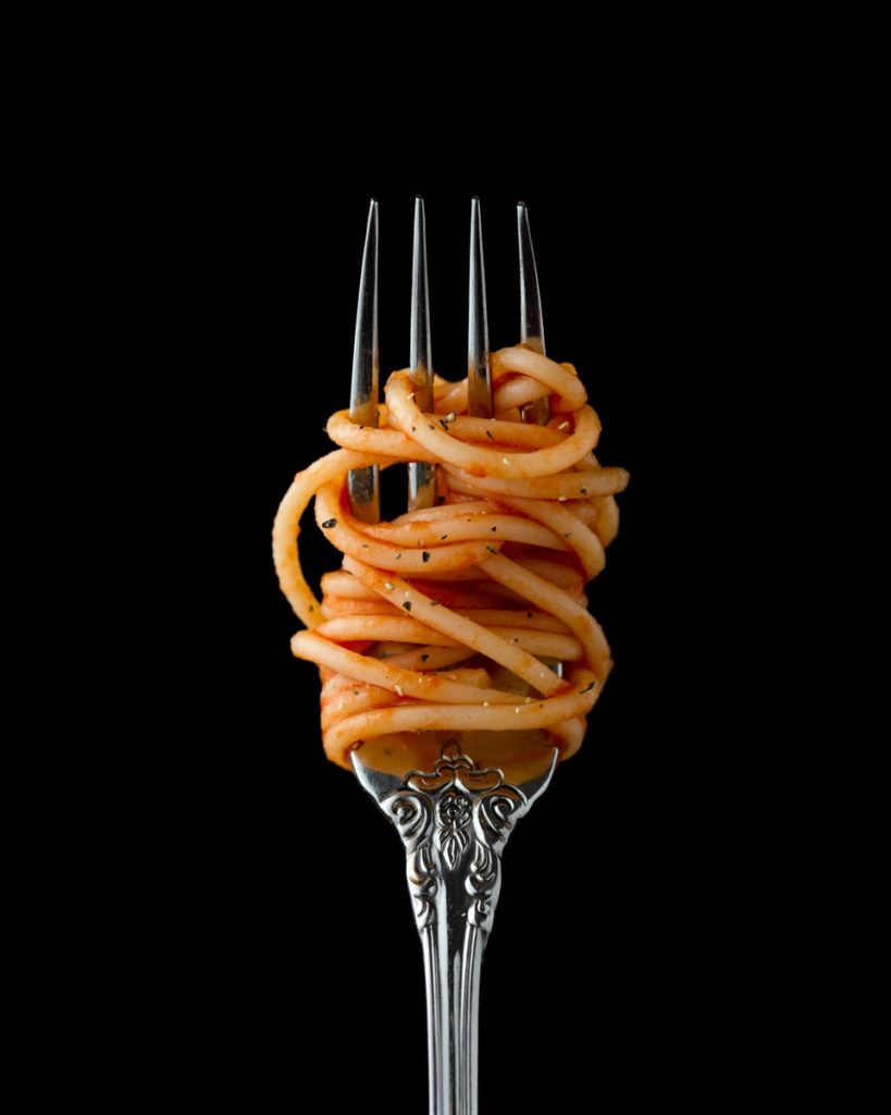 Silver fork with spaghetti with pasta sauce wrapped around fork prongs.