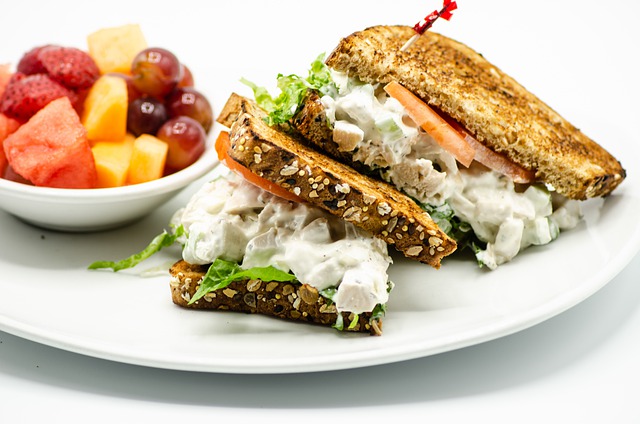 Chicken salad sandwich on a plate with a bowl of fruit. Easy chicken salad recipe for a crowd!