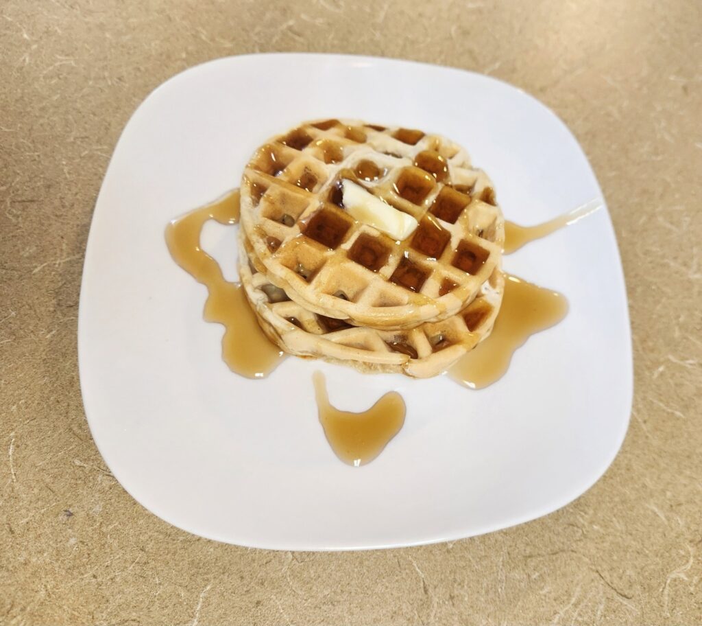 Waffle recipe, white plate with two homemade waffles sitting on it with butter and syrup on top of the homemade waffles.